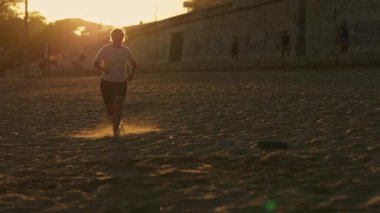 Kararlı kadın altın saat boyunca kumsalda koşuyor.