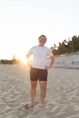 Antrenmandan sonra kumsalda mola veren mutlu bir sporcu. Gün batımının tadını çıkarıyor ve gülümsüyor.