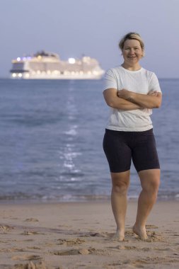 Turistler kumsalda tatilin tadını çıkarırken yolcu gemisi alacakaranlıkta denize açılıyor.