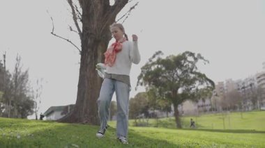 Sarışın kadın parkta yeşil bir şemsiye açıyor.