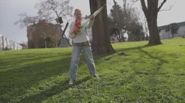 Sarışın kız parkta kırık bir şemsiyeyle eğleniyor.