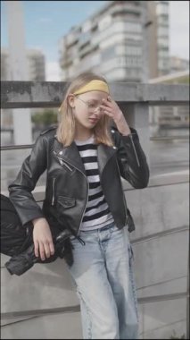 Modern binaların yakınında elinde kaykayla bekleyen şık bir öğrenci.