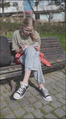 Bankta otururken notlar yazan konsantre öğrenci kız.