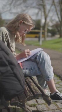 Not defterine konsantre öğrenci yazısı parktaki bankta oturuyor.