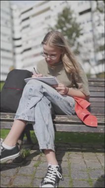 Not defterine konsantre öğrenci yazısı bankta oturuyor.