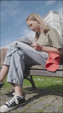 Parktaki bankta otururken not defterine konsantre öğrenci çizimi