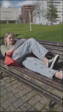 Öğrenci kız şehir parkında bankta uzanıyor, dışarıda yazıyor ve çalışıyor.