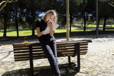 Parktaki bankta oturan not defterine notlar yazan genç öğrenci kız.