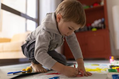 Anaokulu öğrencisi yerde elleri ve renkleri ile resim yaparken eğleniyor.
