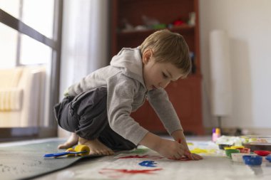 Anaokulu öğrencisi evde yerde canlı renklerle resim yaparken eğleniyor.