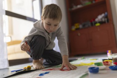 Yaratıcı oyun zamanını seven, parmaklarıyla resim yapan, kağıt üzerinde fırça kullanan, renkleri keşfeden ve evde sanatsal beceriler geliştiren genç bir çocuk.