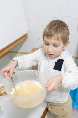 Genç bir çocuk mutfakta yemek pişirirken kasede malzemeleri karıştırıyor, aşçılık becerilerini öğreniyor.