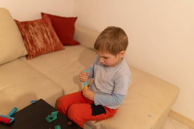 Renkli modelleme kiriyle oynamaya odaklanan genç çocuk, rahat bir ev ortamında yaratıcılığı ve iyi motor becerileri artırıyor.