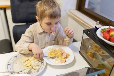 Ufaklık erişte ve sosis yiyor, yanında çilek ve akvaryum var.