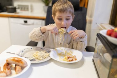 Küçük çocuk evcil mutfak ortamında erişte, sosis ve patates püresi yemekten zevk alıyor.