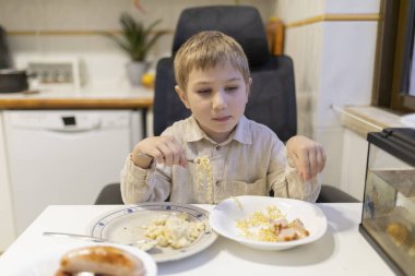 Parlak mutfakta jambonlu erişte ve patates püresi yiyen küçük çocuk.