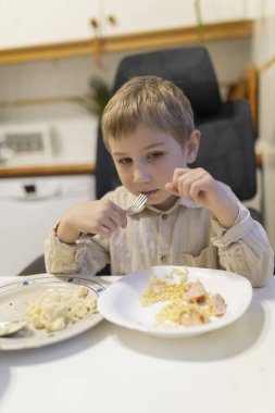 Küçük çocuk öğle yemeğinde sosisli makarna yiyor.