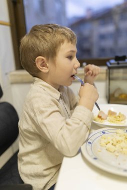 Küçük çocuk makarna, jambon ve peynirin tadını çıkarıyor, çocuklar için sağlıklı beslenme alışkanlıklarını teşvik ediyor.