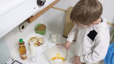 Çocuk malzemeleri bir kasede çırpıyor, mutfakta yemek tarifi hazırlıyor.