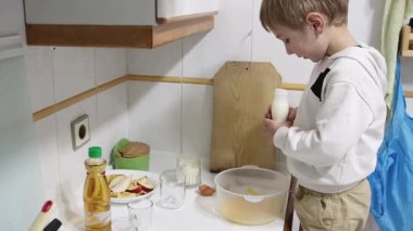 Çocuk yemek yapmayı öğreniyor. Kek yapmak için kaseye süt koyuyor.