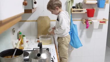 Çocuk kaseye malzeme ekler, evde yemek hazırlar.