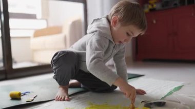 Anaokulu öğrencisi yaratıcı oyun zamanını seviyor, yerde sarı boya ile resim yapıyor.