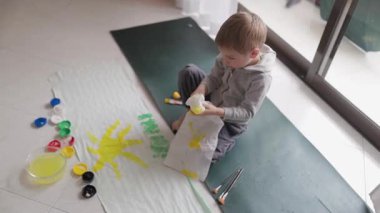 Genç çocuk beyaz bir çarşaf üzerinde güneş yaratmak için sarı boya ve şişe kapağı kullanıyor.