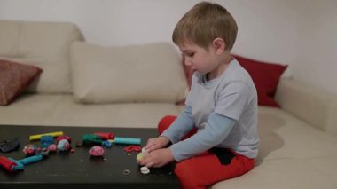 Çocuk yaratıcı oyun zamanını seviyor, kanepenin önündeki masada renkli mankenlik killerini şekillendiriyor.