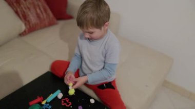 Genç çocuk yaratıcı oyun zamanını seviyor. Masada renkli mankenlik killerini şekillendiriyor.