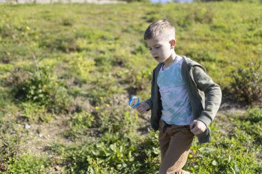 Genç bir çocuk elinde büyüteçle çayırda koşuyor ve doğayı inceliyor.