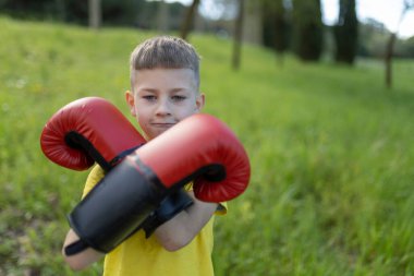 Çocuk parkta boks yapıyor, kırmızı boks eldivenleri giyiyor, sağlıklı yaşam tarzını ve açık hava aktivitelerini destekliyor.