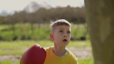 Boks antrenmanı yapan bir çocuk parkta ağaca yumruk atıyor.