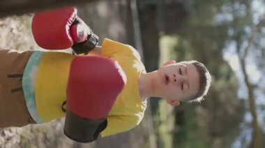 Boksör çocuk dışarıda boks yapıyor, boks eldiveni giyiyor.