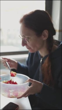 Kızıl saçlı kadın taze sebze salatası yiyor.