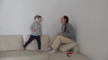 Kulaklıklı enerjik çocuk rahat bir kanepede annesiyle etkileşime geçiyor.