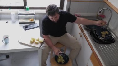 Adam kasede patates soyuyor, modern bir mutfakta taburede oturuyor.