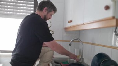 Parlak bir mutfakta bulaşık yıkayan bir adam.