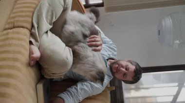 Kanepede oturan ve tüylü kedisini okşayan bir adam.