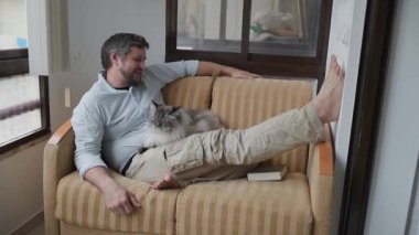 Erkekler kanepede sessizce vakit geçirir, yumuşacık kedisini okşar.