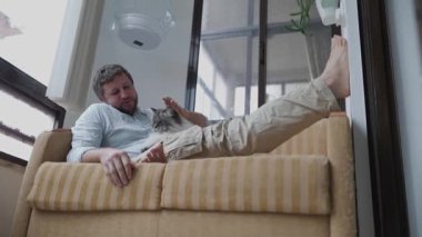 Rahat bir adam kanepede oturup kedi arkadaşıyla vakit geçirmekten hoşlanır.