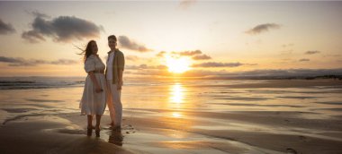 Islak kumda duran iki kadın, okyanusun üzerinde altın bir günbatımının tadını çıkarıyorlar.