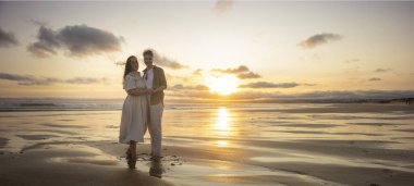 Gün batımında güzel bir sahilde sarılıp el ele tutuşan iki kadın.