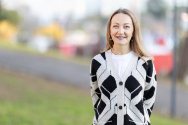 Diş teli takan gülümseyen bir kadın dışarı çıkıp kameraya bakıyor.