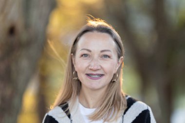 Dışarıda duran kadın, izleyiciye doğru gülümsüyor, diş teli takıyor.