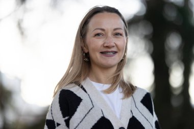 Diş teli takan gülümseyen kadın açık hava ortamında doğrudan izleyiciye bakıyor.