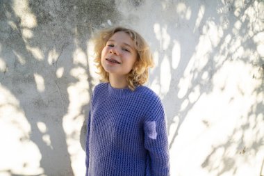 Mor kazaklı sarışın ergen kız, dışarıda güneş ışığıyla gülümsüyor.