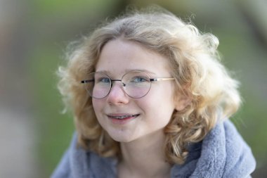 Gülümseyen ve ileriye bakan genç bir kız, diş tellerini ve gözlüklerini gösteriyor.