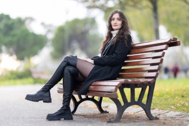 Parktaki bankta oturan genç bir kadın şık bir şekilde poz veriyor.