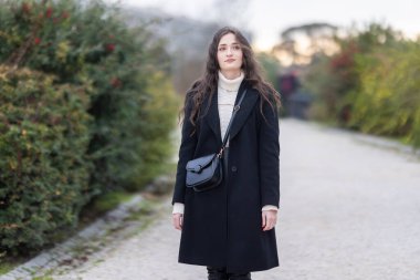 Bir kadın yolda dikiliyor, düşünceli bir ifadeyle yukarı bakıyor.