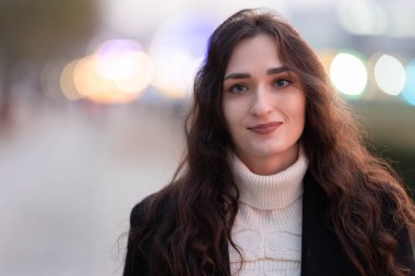 Kameraya bakan genç bir kadın, arka planda Bokeh ışıkları ile güvenle gülümsüyor.